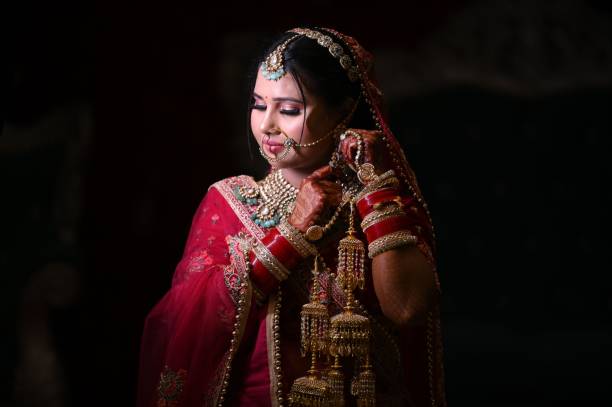 A beautiful Indian bride in traditional red attire and jewelry, adjusting her earrings.